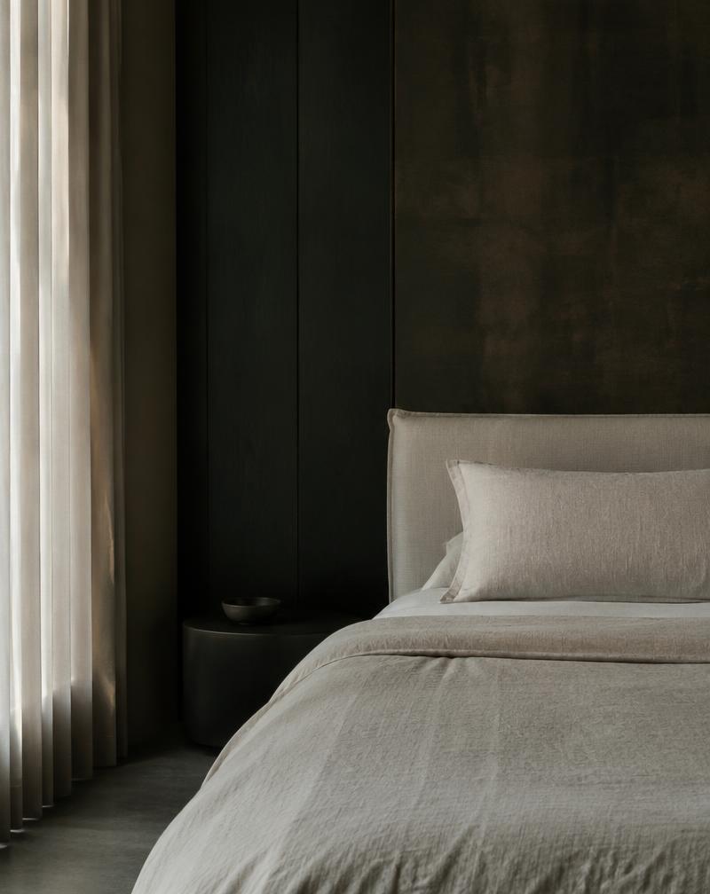 Linen bed in a dark suite lit by soft window light